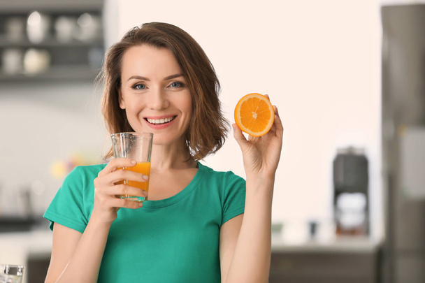 Mooie vrouw met glas Gezond sap van citrusvruchten en oranje helft in keuken - Foto, afbeelding