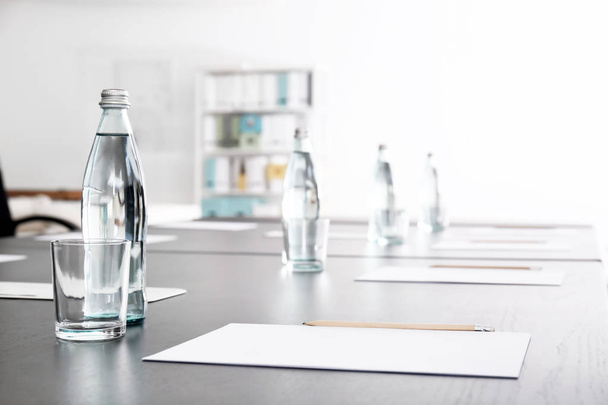 Стол с бутылками воды и листами бумаги, подготовленный для деловой встречи в конференц-зале
 - Фото, изображение