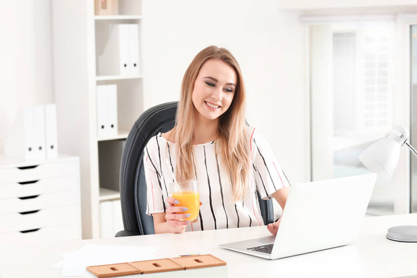 Όμορφη νεαρή γυναίκα πίνοντας χυμό εσπεριδοειδών στο γραφείο - Φωτογραφία, εικόνα