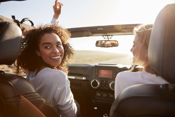 Two girlfriends driving with sunroof open, one turning round - Valokuva, kuva
