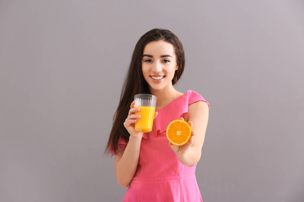 Όμορφη νεαρή γυναίκα με ποτήρι χυμό εσπεριδοειδών και φρούτων σε γκρίζο φόντο - Φωτογραφία, εικόνα