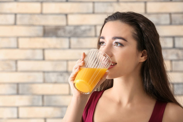 Beautiful young woman drinking citrus juice against brick wall - Foto, afbeelding