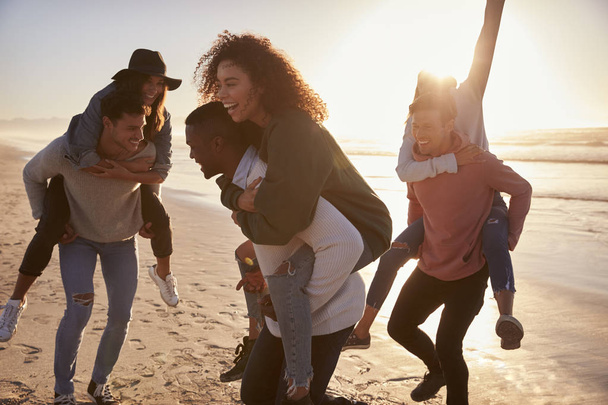 Group Of Friends Having Piggyback Race On Winter Beach Together - Photo, image
