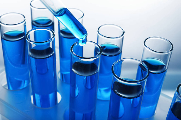 tropft blaue Flüssigkeit in Reagenzgläser auf hellem Hintergrund - Foto, Bild