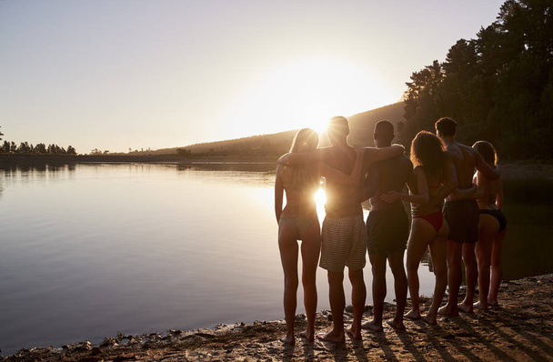 Молодые взрослые друзья тусуются на берегу озера, вид сзади
 - Фото, изображение