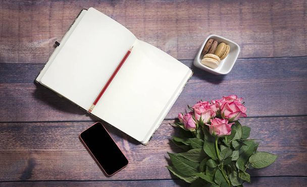 Top view of blank sheet of notebook and red and pink roses flowers on rustic brown wooden table. Copy space. Flat lay, top view office table desk. feminine desk workspace with roses, diary.  - Photo, image