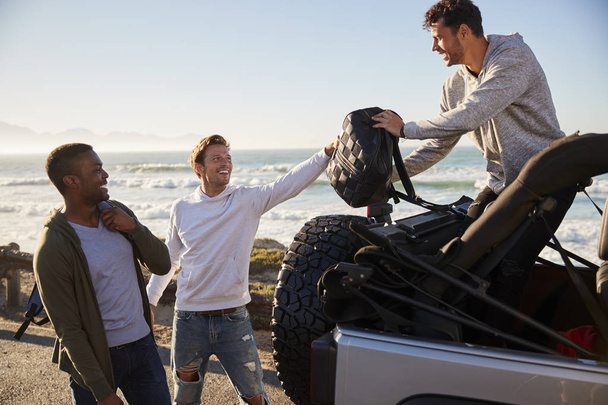 Three young adult male friends unloading backpacks from jeep - Foto, immagini