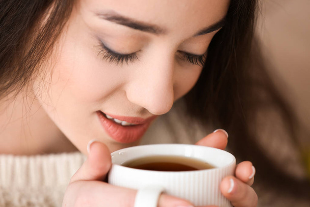Beautiful young woman with cup of hot tea at home, closeup - Foto, immagini