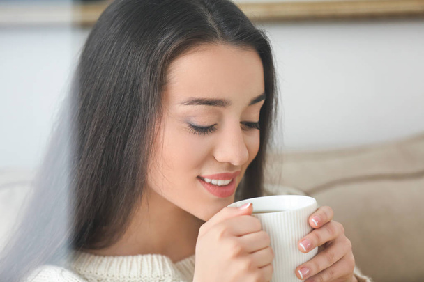 Mulher bonita com xícara de chá quente em casa, vista através da janela
 - Foto, Imagem