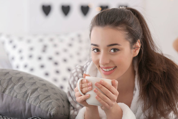 Beautiful young woman with cup of hot tea at home - 写真・画像