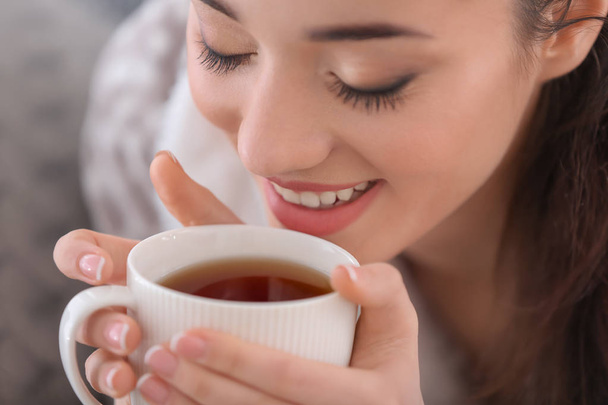 Beautiful young woman with cup of hot tea at home, closeup - Zdjęcie, obraz