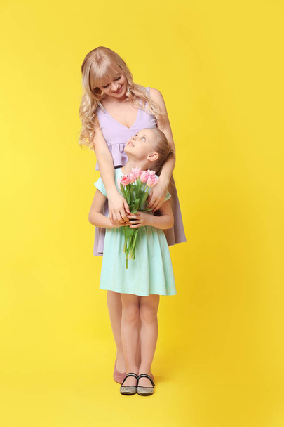 Portrait of cute little girl and her mother with tulip bouquet on color background - Photo, Image