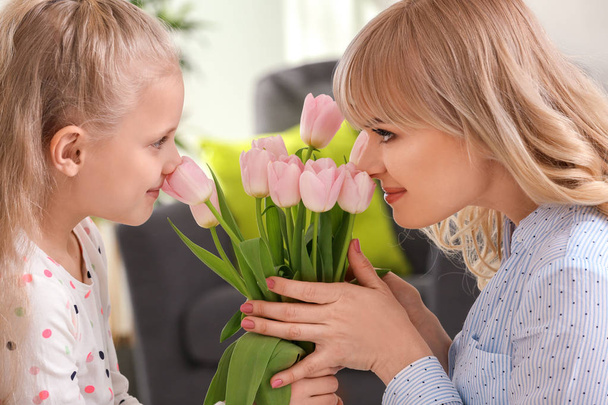 Portrait of cute little girl and her mother with tulip bouquet at home - Foto, Imagem