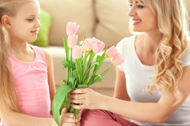 Schattig klein meisje tulip boeket te geven aan haar moeder thuis - Foto, afbeelding