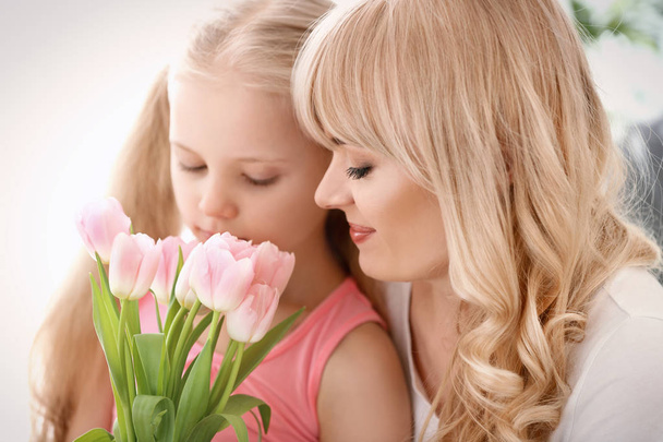 Portret van een schattig klein meisje en haar moeder met tulip boeket op lichte achtergrond - Foto, afbeelding