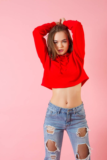 Emotional girl in jeans and a red sweater. Studio portrait - 写真・画像