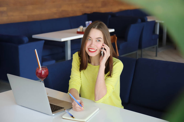 Молодой фрилансер разговаривает по мобильному телефону во время работы с ноутбуком в кафе
 - Фото, изображение