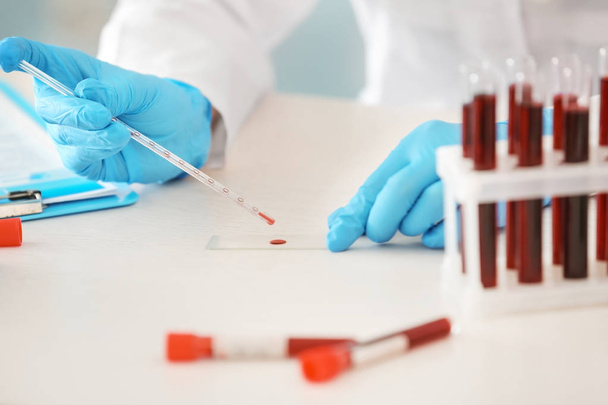 Femme travaillant avec un échantillon de sang provenant d'un tube à essai à table
 - Photo, image