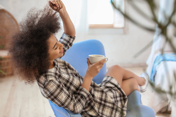 Belle femme afro-américaine buvant du thé dans un fauteuil à la maison
 - Photo, image