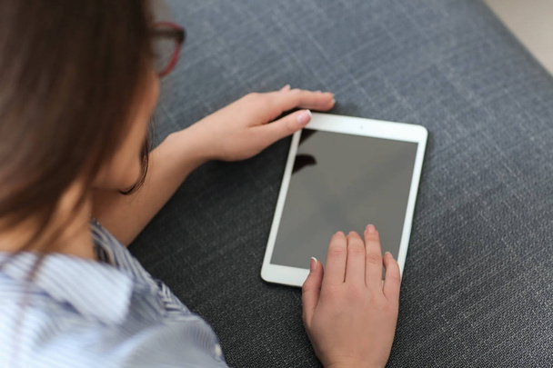 Jeune femme utilisant une tablette tout en se reposant sur le canapé à la maison
 - Photo, image