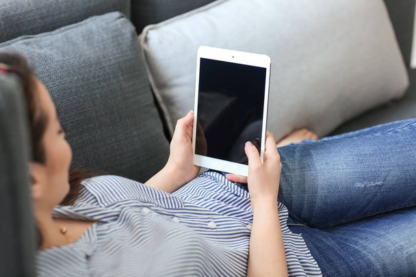 Giovane donna che utilizza tablet mentre si riposa sul divano a casa
 - Foto, immagini