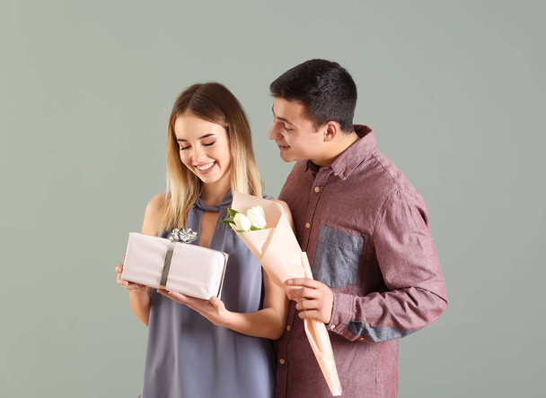 Young man giving present and flowers to his beloved girlfriend on color background - Photo, Image