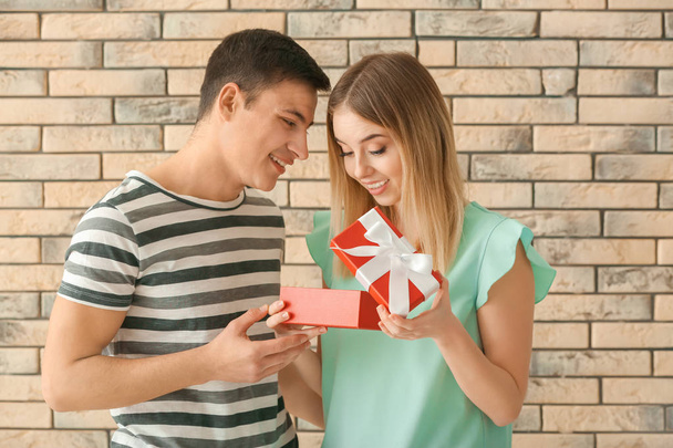 Young woman opening gift box from her boyfriend near brick wall - Foto, imagen