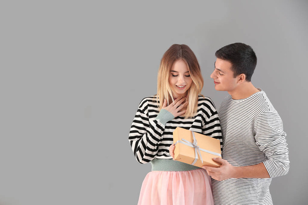Young man giving present to his beloved girlfriend on grey background - Foto, imagen