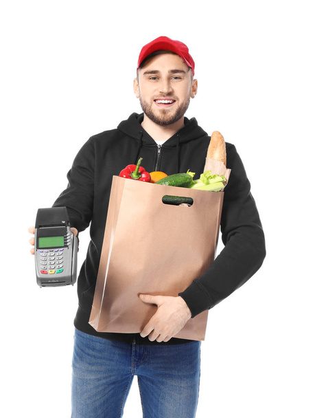 Young man with products in paper bag and bank terminal on white background. Food delivery service - Photo, Image