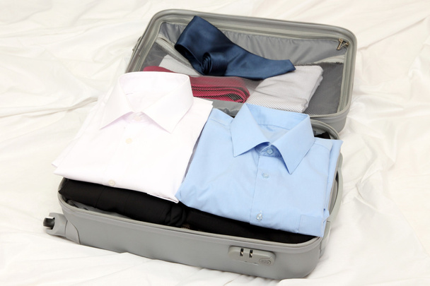 Open grey suitcase with clothing on bed - Φωτογραφία, εικόνα
