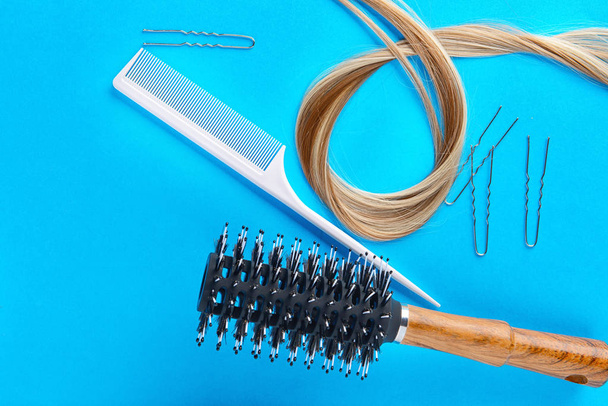 Επίπεδη lay σύνθεση με εργαλεία κομμωτηρίου και το σκέλος του ξανθά μαλλιά στο χρώμα φόντου - Φωτογραφία, εικόνα