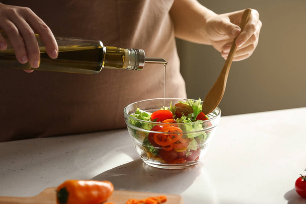 Woman adding olive oil into bowl with fresh vegetable salad on table - Zdjęcie, obraz