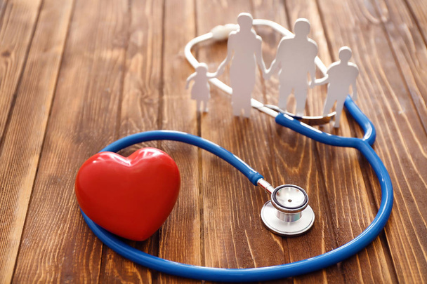 Familienfigur, rotes Herz und Stethoskop auf Holzgrund. Gesundheitskonzept - Foto, Bild