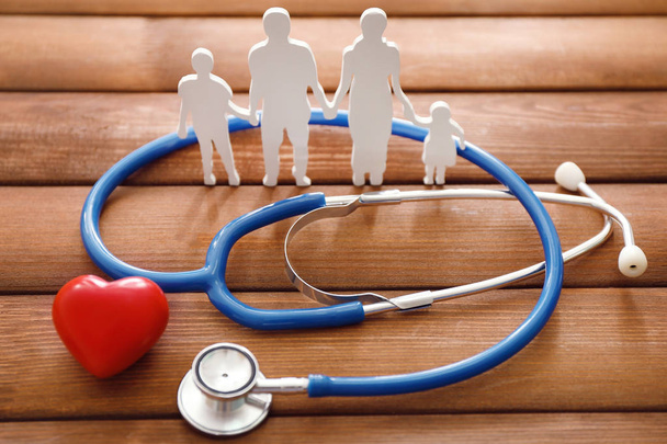 Family figure, red heart and stethoscope on wooden background. Health care concept - Photo, Image