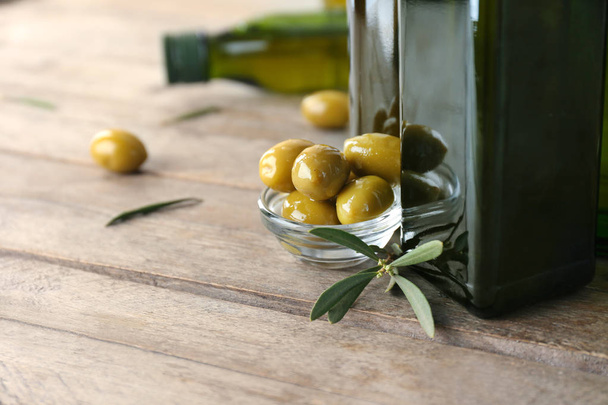 Čerstvé olivy a láhev s olejem na dřevěné pozadí, closeup - Fotografie, Obrázek