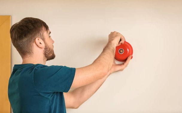 Young man installing alarm bell on wall - 写真・画像