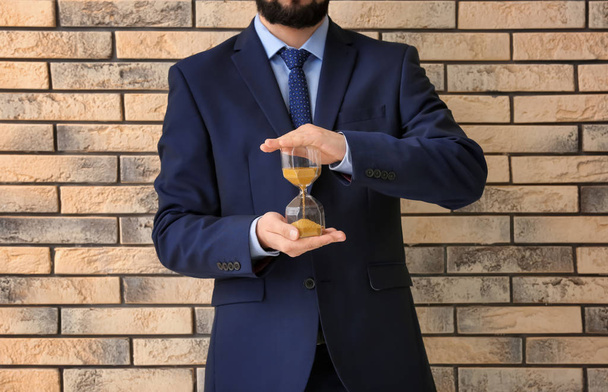 Человек держит песочные часы на кирпичном фоне. Концепция управления временем
 - Фото, изображение