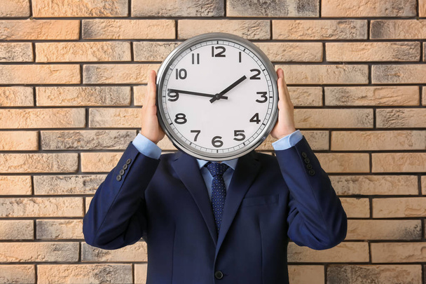Man holding clock on brick background. Time management concept - Фото, зображення