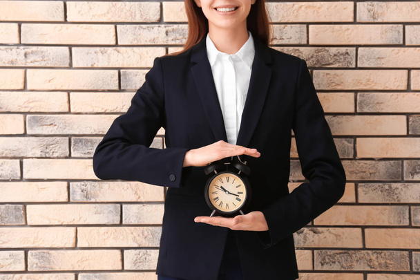Женщина держит будильник на кирпичном фоне. Концепция управления временем
 - Фото, изображение
