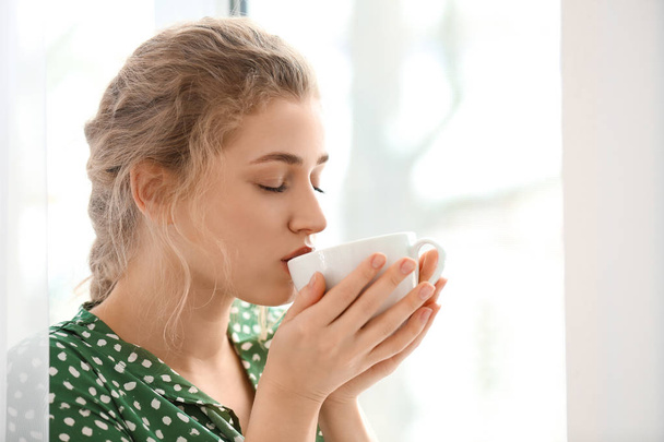 Young woman drinking tea near window indoors - Foto, Imagem