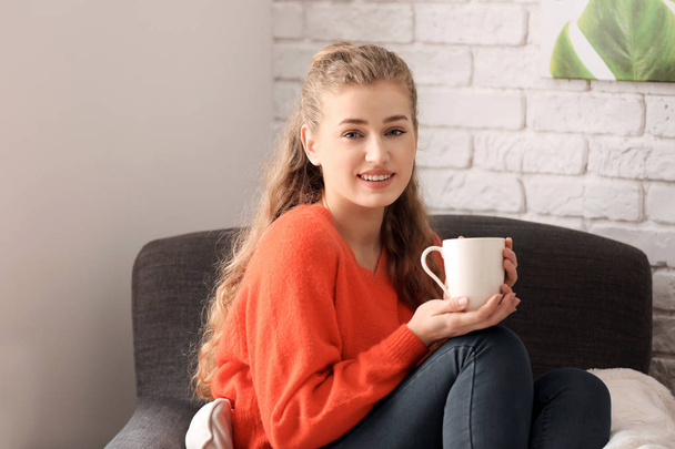 Jeune femme au repos avec une tasse de thé dans le fauteuil à la maison
 - Photo, image