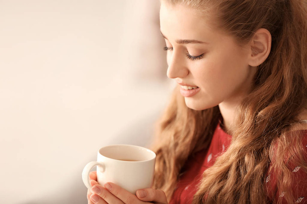 Young woman drinking tea on blurred background - Valokuva, kuva