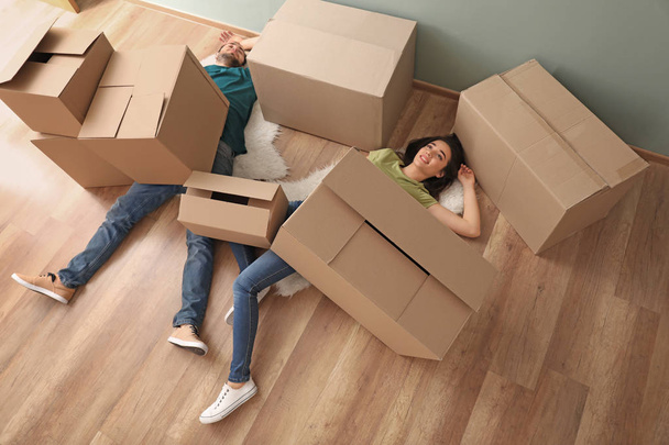Young couple buried under heap of boxes indoors. Moving into new house - Photo, Image