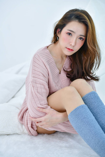 Winter Concept. Cute Asian girl in winter dress. Beautiful woman is relaxing in a white bedroom. Beautiful women in winter clothes are relaxing in the morning. Woman wearing a sweater in a white bedroom. - Foto, imagen