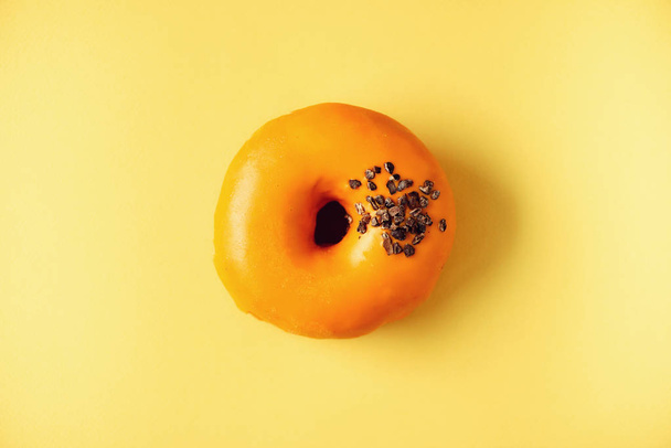 Sweet doughnut with orange glaze and chocolate on grey background. Tasty donut on pastel yellow texture, copy space, top view - Photo, Image