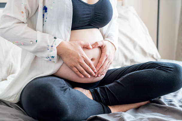 Νέοι όμορφη Ασίας έγκυος γυναίκα κρατώντας τα χέρια της στο ένας ακούει - Φωτογραφία, εικόνα