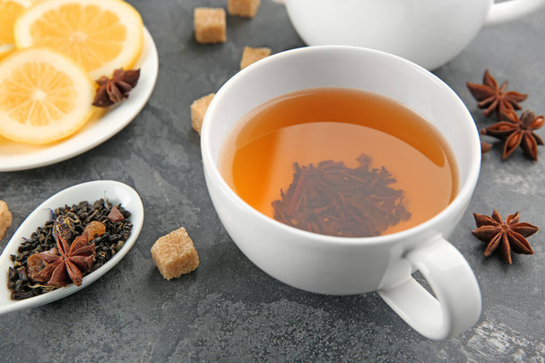Cuchara con hojas de té verde seco y taza de bebida aromática en la mesa
 - Foto, imagen
