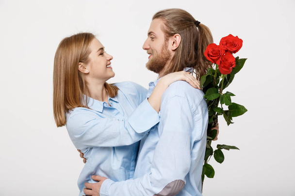 Portrait of an attractive young man hiding flowers from his girlfriend before giving her a surprise over white isolated background. - Photo, Image