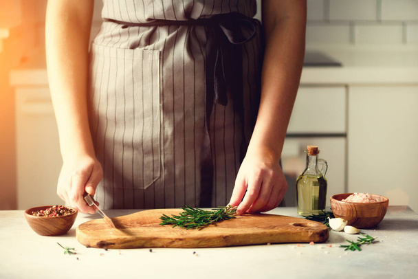 Woman hands cutting fresh green rosemary on wood chopping board in white kitchen, interior. Copy space. Homemade food conceplt, healthy recipe. Take me to work - Foto, afbeelding