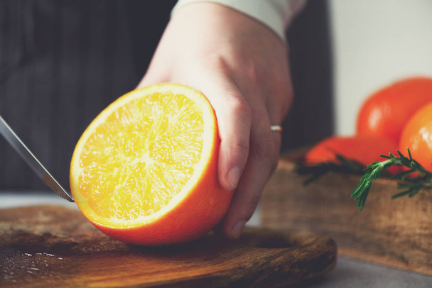 Woman hands slicing orange, cutting citrus fruit. Knife, wooden cutting board on design white kitchen. Copy space - Fotó, kép